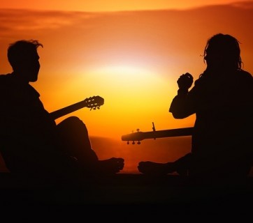 Dwoje ludzie z gitarami siedzących przy zachodzie słońca