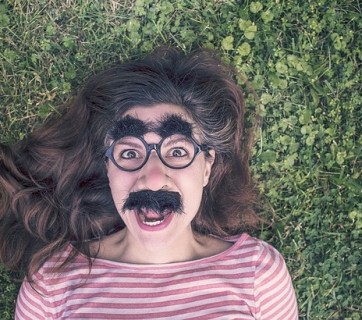 Kobieta leżąca na trawie mająca śmieszne okulary na twarzy