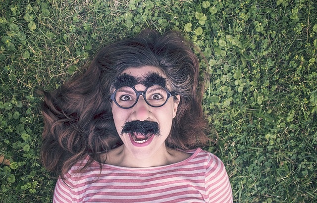 Kobieta leżąca na trawie mająca śmieszne okulary na twarzy
