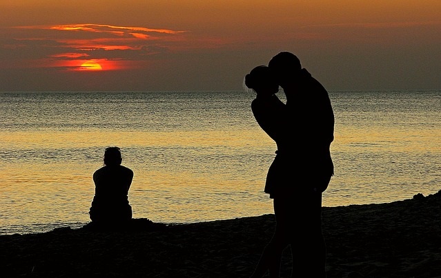Całująca się para i siedzący na plaży samotny człowiek